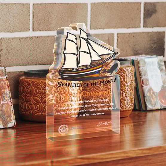 Eight Inch Sailboat Shaped Acrylic Award For Seafarer Printed With Ship Logo And Message Freestanding On Wood Table With Pots