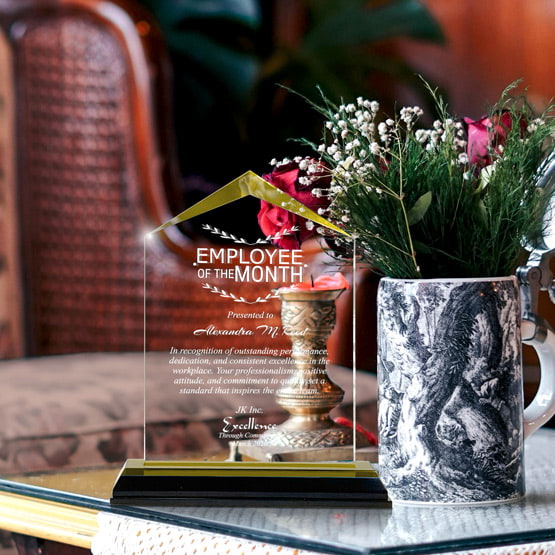 Jewel Impress Acrylic Award For Employee Of The Month With Black And Gold Base On Glass Coffee Table With Potted Flowers