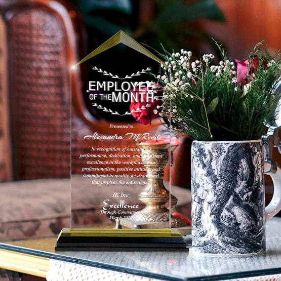 Jewel Impress Acrylic Award For Employee Of The Month With Black And Gold Base On Glass Coffee Table With Potted Flowers