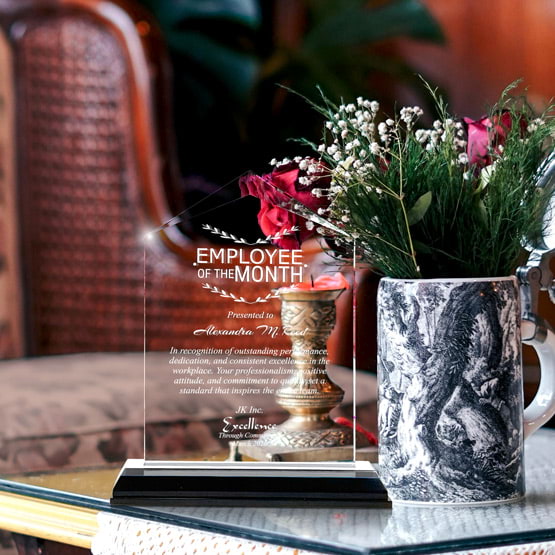 Jewel Impress Acrylic Award For Employee Of The Month With Black And Silver Base On Glass Coffee Table With Potted Flowers