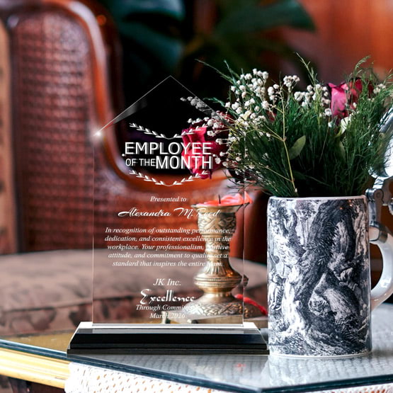 Jewel Impress Acrylic Award For Employee Of The Month With Black And Silver Base On Glass Coffee Table With Potted Flowers