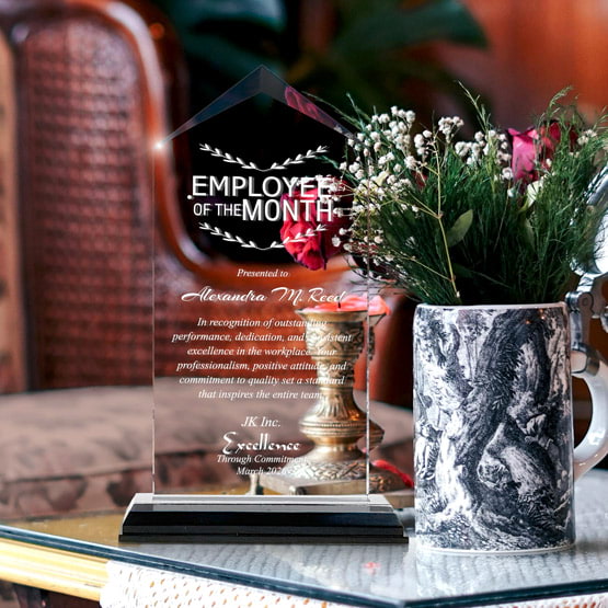 Jewel Impress Acrylic Award For Employee Of The Month With Black And Silver Base On Glass Coffee Table With Potted Flowers