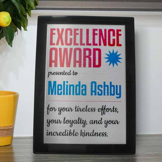 Custom Black Piano Finish And Silver Aluminum Plaque Award For Excellence On A Wood Shelf With Small Potted Lemon Tree