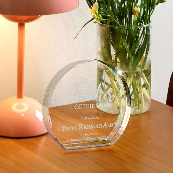 Freestanding Circle Glass Award Engraved With Teacher Of The Year Message On Wood Desk With Flowers And Lamp