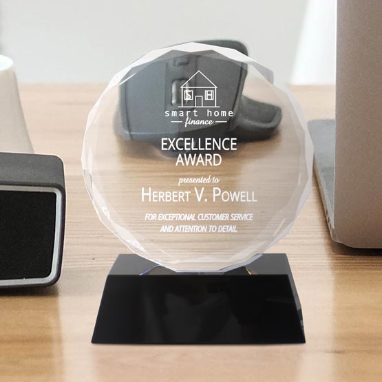 Custom Faceted Circle Glass Award For Excellence Standing Via Black Base On Wood Work Desk With Laptop And Mouse And Clock