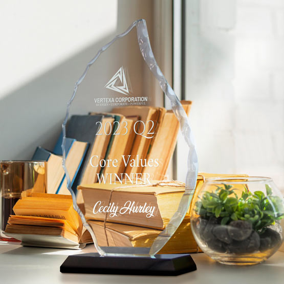 A clear glass award in a flame shape, displayed on a black base on a desk. The award is as engraved text about an award for a ‘Core Values Winner’ to ‘Cecily Hurley’.