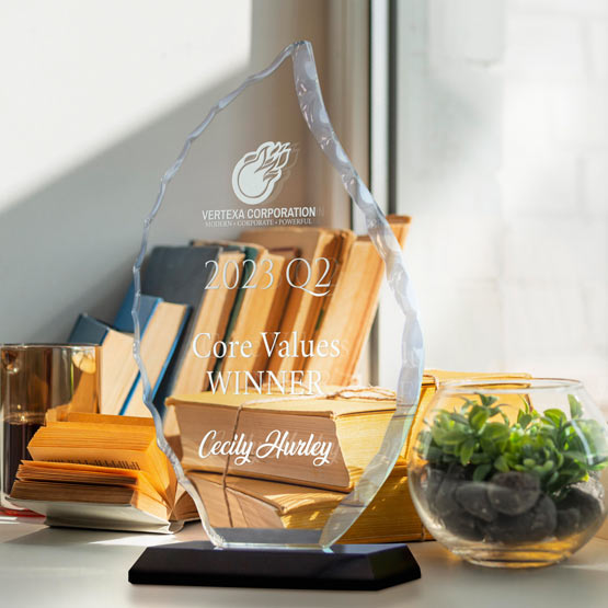A clear glass award in a flame shape, displayed on a black base on a desk. The award is as engraved text about an award for a ‘Core Values Winner’ to ‘Cecily Hurley’.