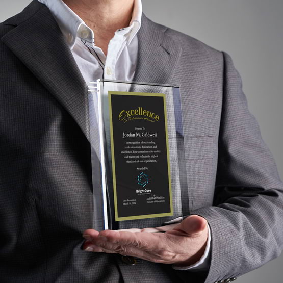 Man In Business Suit Holding Rectangle Glass Award With Black Screen Printed With Excellent Performance Message And Logo