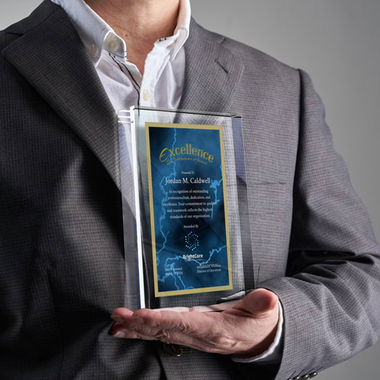 Man In Business Suit Holding Rectangle Glass Award With Blue Screen Printed With Excellent Performance Message And Logo
