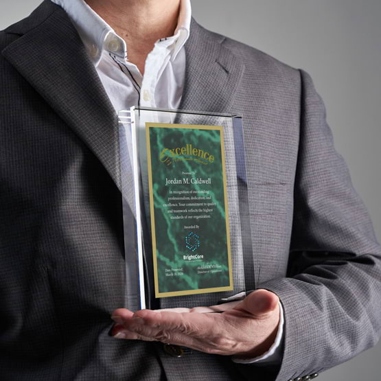 Man In Business Suit Holding Rectangle Glass Award With Green Screen Printed With Excellent Performance Message And Logo
