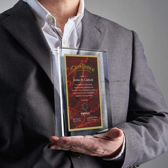 Man In Business Suit Holding Rectangle Glass Award With Red Screen Printed With Excellent Performance Message And Logo