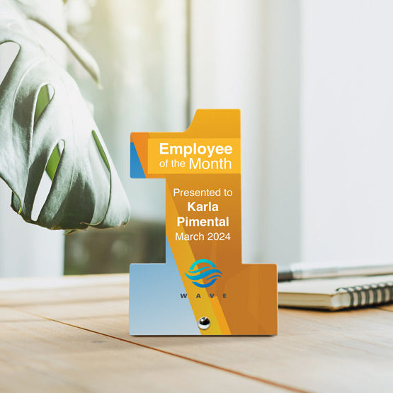 Number One Shaped Stainless Steel Award Printed With Employee Of The Month Message On Wood Desk With Plant And Notepad