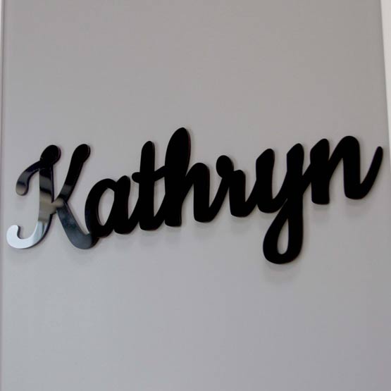 Custom Black Acrylic Sign Featuring Cursive Cutout Of The Name Kathryn Hanging On A White Living Room Wall
