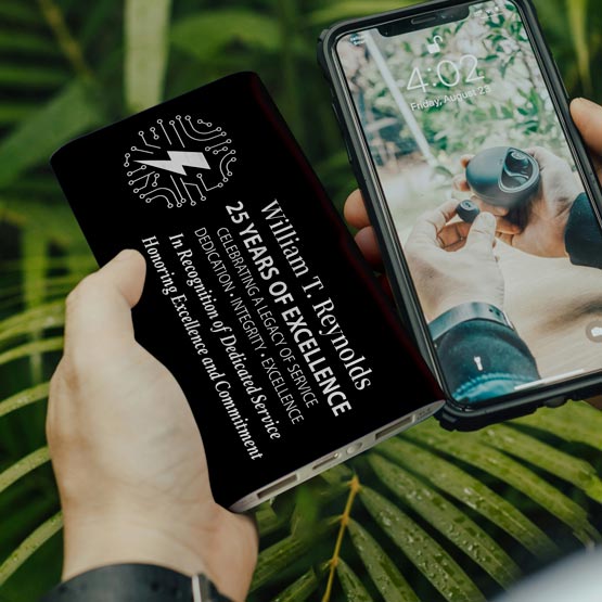 Hands Outdoors Holding A Black Aluminum Power Bank Custom Engraved With Tech Logo And Years Of Service Award Message