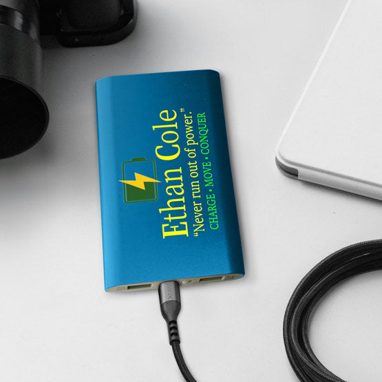 Blue Aluminum Power Bank Custom Printed With Logo And Name And Motto Charging A Laptop Via USB C Cable On Office Desk