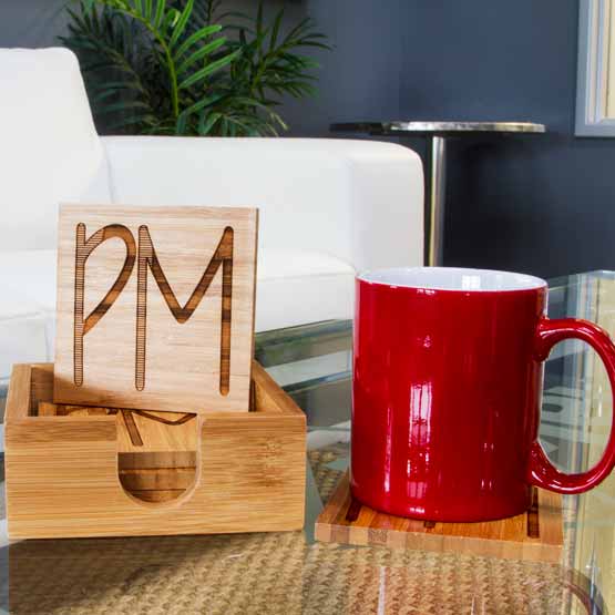 Set Of Four Custom Bamboo Coasters In Case On A Glass Coffee Table With Red Coffee Mug In Living Room Near Couch