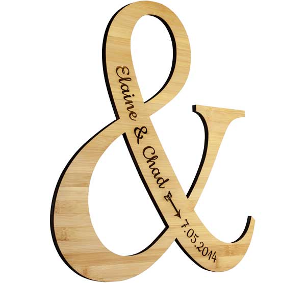 Custom Ampersand Shaped Bamboo Sign And Laser Engraved With Couple Names And Full Date Against A White Background