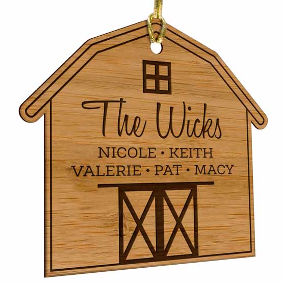 Custom Barn Shaped Bamboo Ornament Laser Engraved With Family Names And Gold String Against A White Background