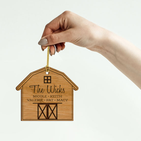 Woman Hand Holding Up Custom Barn Shaped Bamboo Ornament Laser Engraved With Family Names Via Gold String