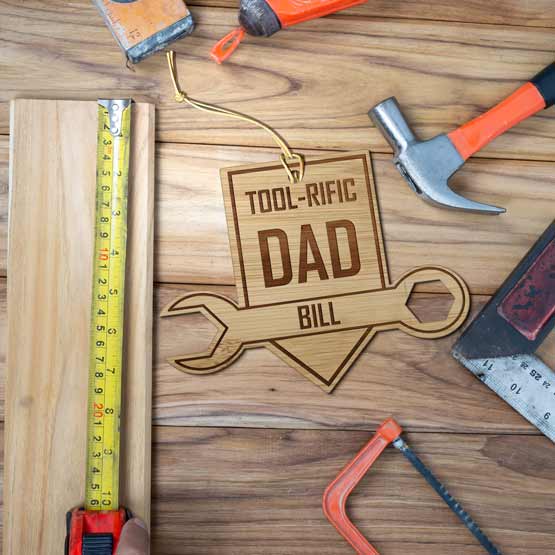 Custom Wrench On Sign Shaped Bamboo Ornament Engraved With Name And Tool-Riffic Dad Text On A Workbench With Handiwork Tools