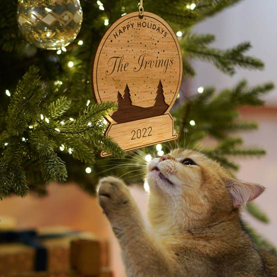 Cat Playing With Custom Snow Globe Bamboo Ornament Engraved With Happy Holidays And Family Name Hanging On Christmas Tree