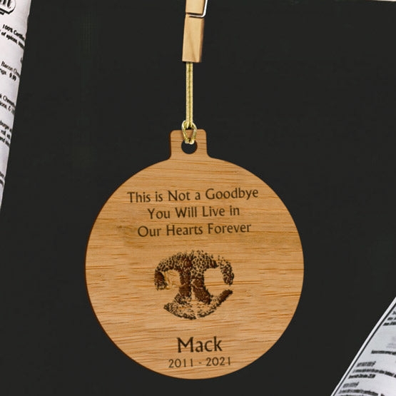 Custom Circle Bamboo Ornament With Gold String And Engraved With Dog Nose Artwork And Memorial Message On A Black Table