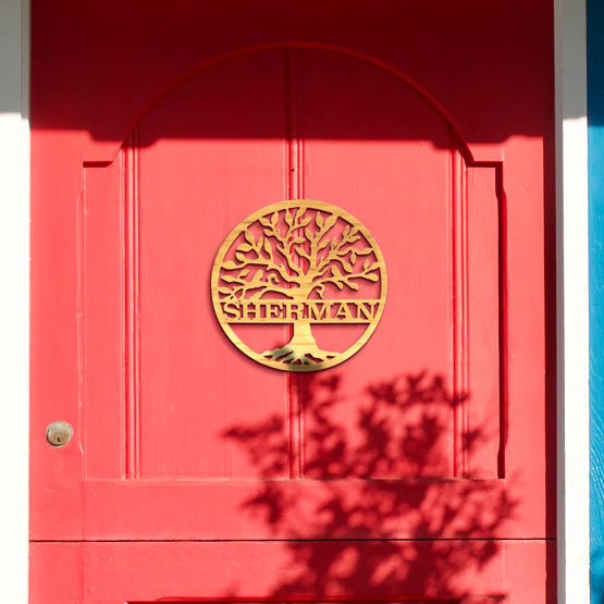 Custom Circle Bamboo Sign With Detailed Cutout Of Tree And Family Name Hanging Outside On A Red Door At Front Porch
