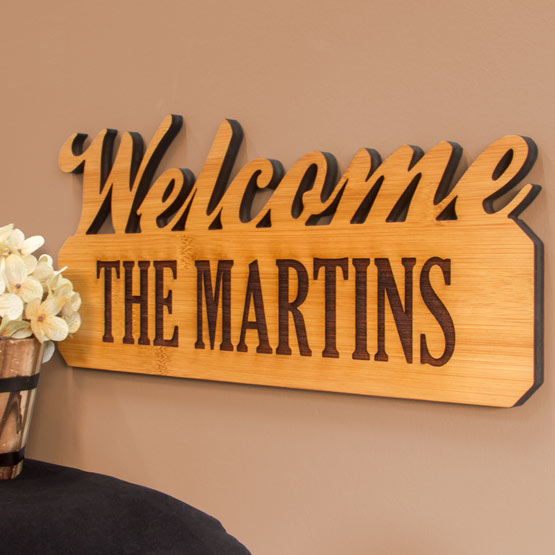 Custom Bamboo Sign With Welcome Cutout And Engraved With The Martins Hanging On Living Room Wall Near Flower Pot