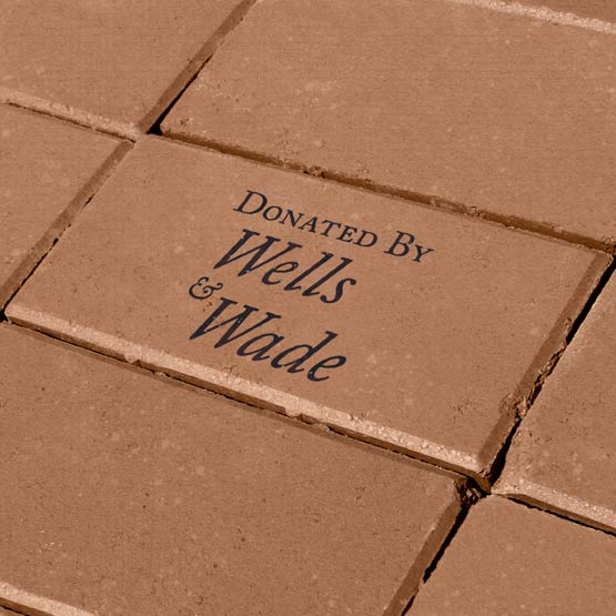Custom Paver Brick Laser Engraved With Donated By Wells And Wade Sitting In The Ground With Matching Blank Bricks