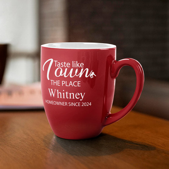 A red ceramic coffee mug featuring personalized white engraved text that reads ‘Taste like I Own THE PLACE Whitney HOMEOWNER SINCE 2024’, sitting on a wooden table in a warm, blurred indoor setting.