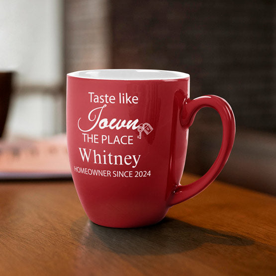A red ceramic coffee mug featuring personalized white engraved text that reads ‘Taste like I Own THE PLACE Whitney HOMEOWNER SINCE 2024’, sitting on a wooden table in a warm, blurred indoor setting.
