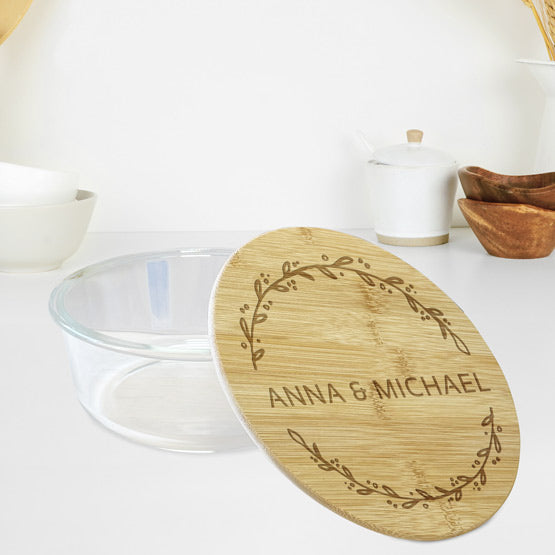 Custom Round Glass Baking Dish With Bamboo Lid Engraved With Couple Names And Wheat Art Sitting On White Counter With Bowls