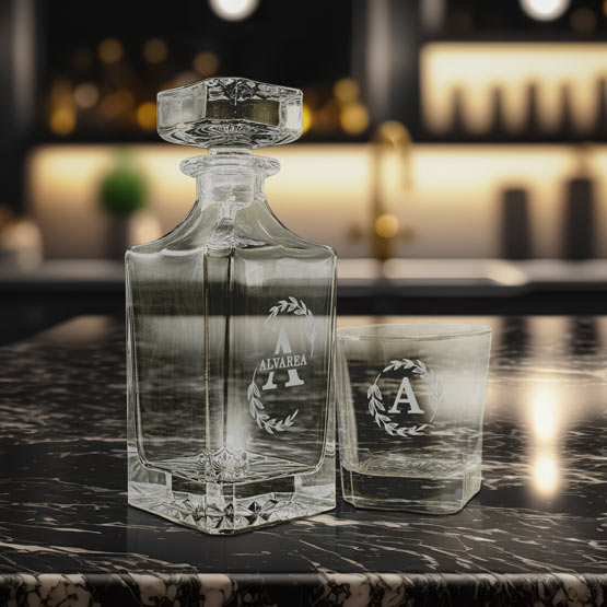 Custom Glass Decanter With Stopper Engraved With Alvarea Logo Beside Matching Rocks Glass On A Marble Bar Counter