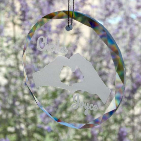Circle Glass Suncatcher Engraved With Couple Names And Hands Making Heart Artwork Hanging By Window With Flowers Outside