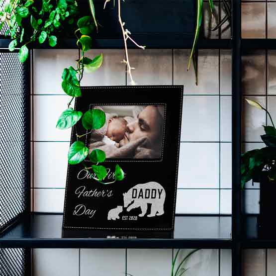 Custom Black Faux Leather Picture Frame With First Father’s Day Text And Bear Artwork And Family Photo On Shelf With Plants