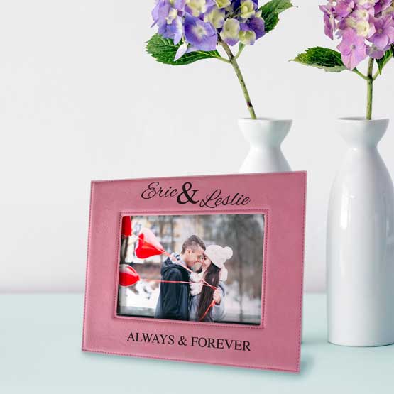 Custom Pink Faux Leather Picture Frame With Couple Photo And Always And Forever Text On A White Shelf With Flowers In Vases