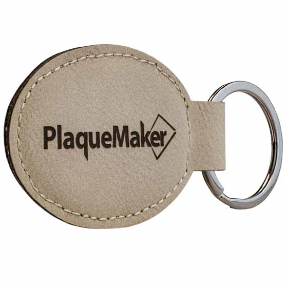 Custom Light Brown Faux Leather Oval Keychain Laser Engraved With PlaqueMaker Logo Against A White Background