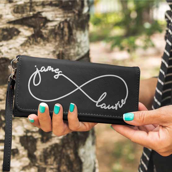 Woman Hands Outdoors Holding Black Faux Leather Trifold Wallet With Wrist Strap And Engraved With Connected Couple Names