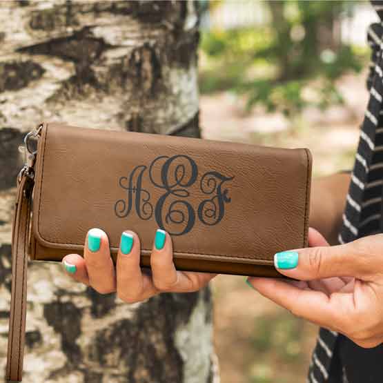 Woman Hands Outdoors Holding Dark Brown Faux Leather Trifold Wallet With Wrist Strap And Engraved With Ornate Initials