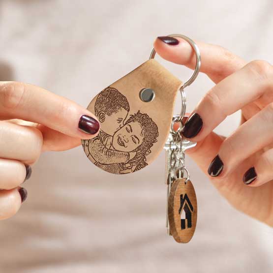 Woman Hands Holding House Keys And Custom Light Brown Leather Teardrop Keychain Engraved With Mom Holding Child Art 