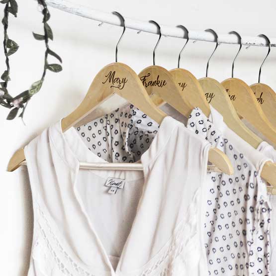 Row Of Custom Maple Wood Clothes Hangers Holding White Dresses And Engraved With Names Hanging On Rod In White Closet