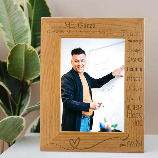 Red Alder Picture Frame With Teacher Photo And Engraved With Teacher Details And Traits And Learn On White Shelf Beside Plant