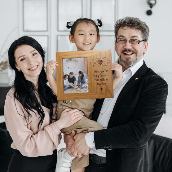 Parents Holding Up Girl With Red Alder Picture Frame With Family Photo And Mom Inside Puzzle Piece Art And Thank You Message