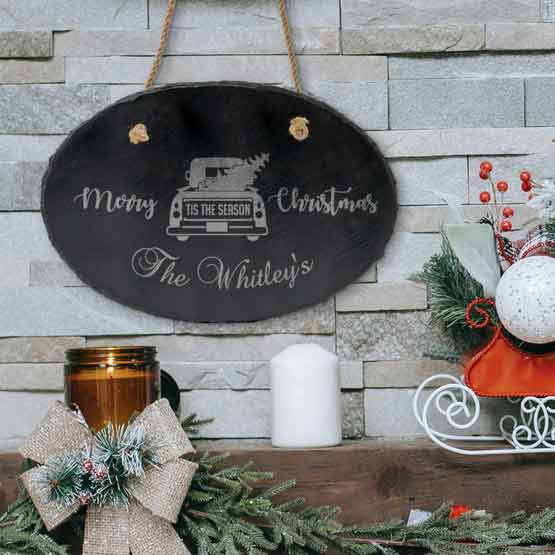 Slate Oval Sign Printed With Merry Christmas And Family Name And Festive Truck Art Hanging Above Decorated Shelf Via Rope