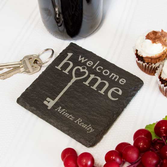 Slate Square Coaster Printed With Welcome Home And Mintz Realty And Key Artwork On White Table With House Keys And Food