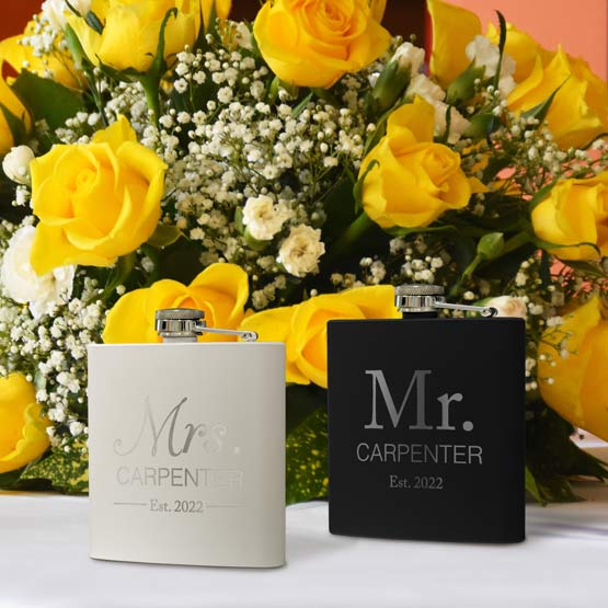 Pair Of Black And White Stainless Steel Flasks Featuring Mister And Misses Carpenter And Date On White Table With Flowers