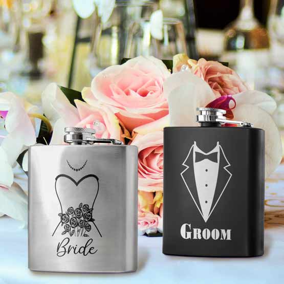 Set Of Black And Silver Stainless Steel Flasks Featuring Groom And Tuxedo And Bride And Dress On Table With Flowers