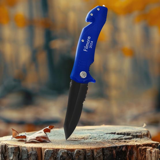 Custom Blue Stainless Steel Rescue Knife In Open Position And Laser Engraved With Filmore 2024 And Piercing A Log Outdoors
