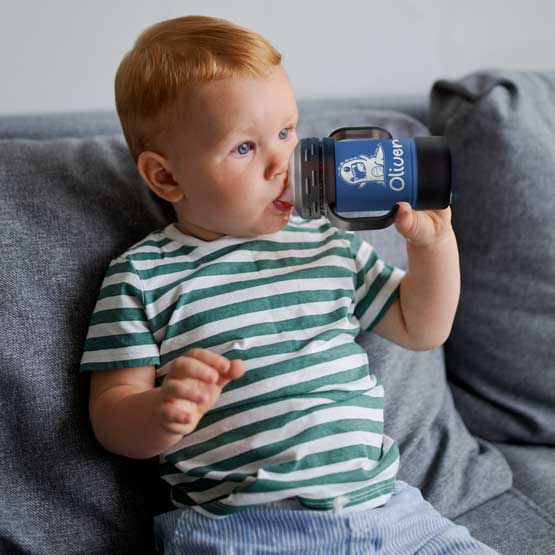 Child On Couch Drinking From Custom Blue Stainless Steel Sippy Cup With Handles And Engraved With Name And Cute Clipart