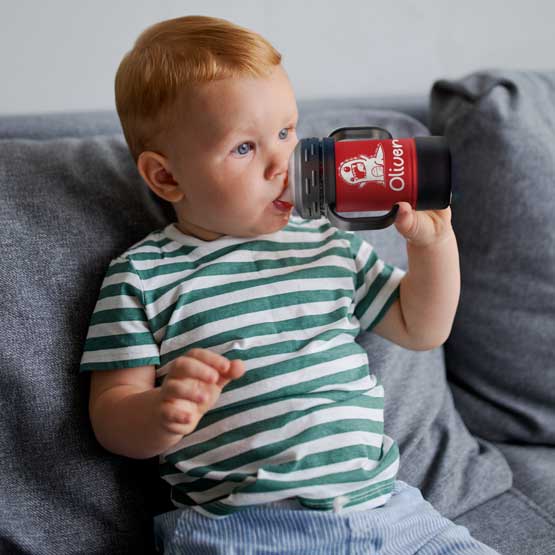 Child On Couch Drinking From Custom Red Stainless Steel Sippy Cup With Handles And Engraved With Name And Cute Clipart